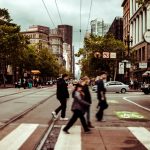 Pedestrians crossing a busy intersection in downtown San Francisco on a cloudy day.