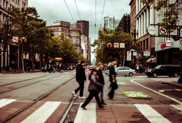 Pedestrians crossing a busy intersection in downtown San Francisco on a cloudy day.